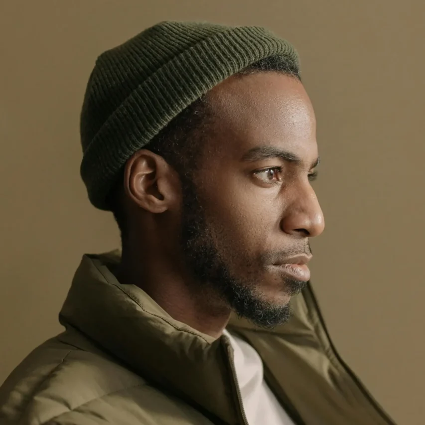 Portrait of an adult man in a beanie looking to the side with a calm expression against a plain background.